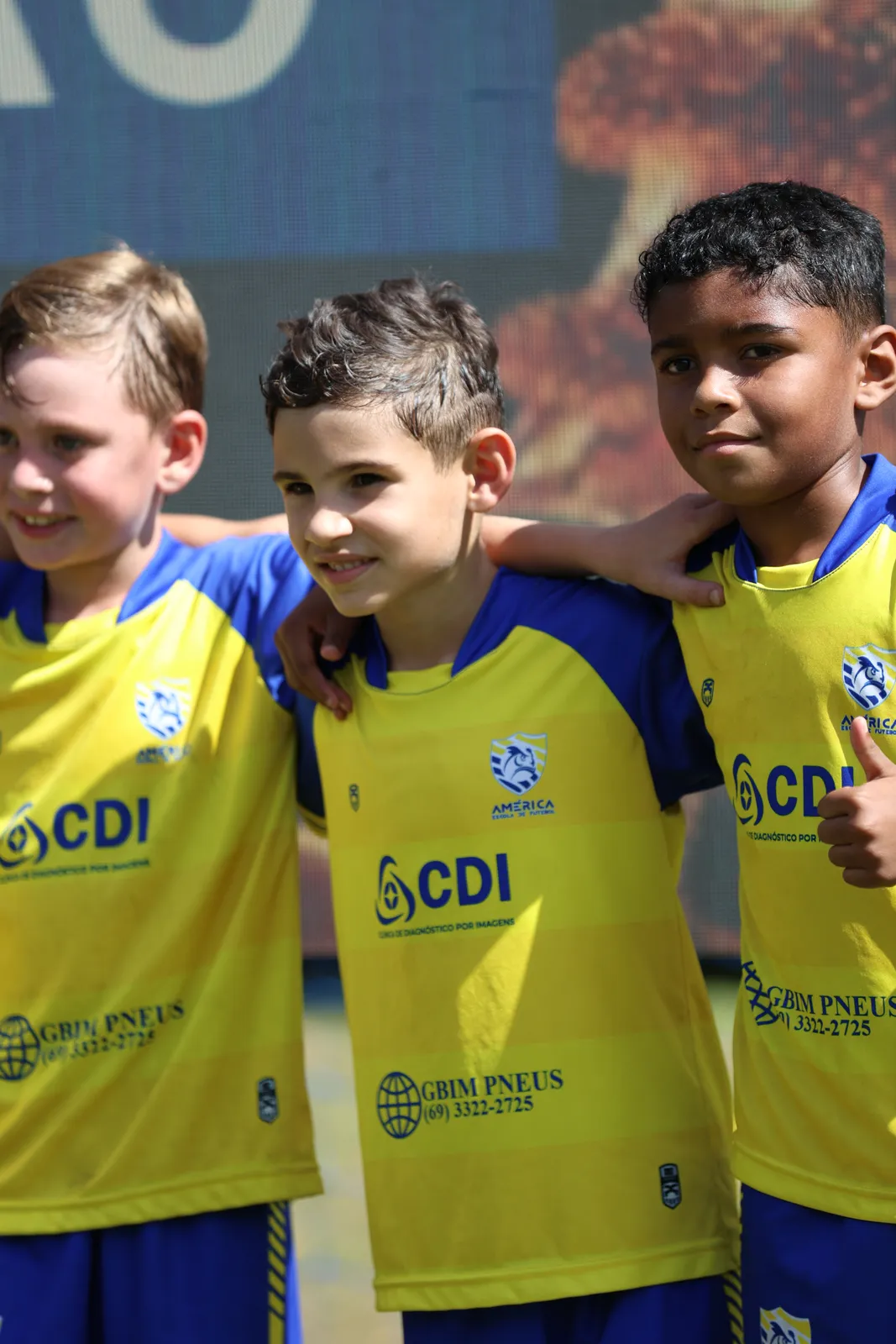 Três alunos da América abraçados e sorrindo com o uniforme amarelo